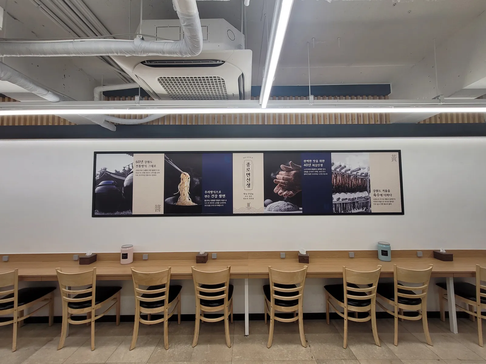 벽돌 기둥 옆 바 좌석과 면 요리 벽화가 있는 종로 면선생 내부